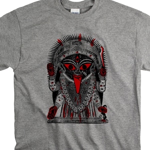 May include: A grey t-shirt with a graphic of a deity with red eyes, a long red tongue, and detailed jewellery. The design is mainly black and red, with a stylized appearance. The shirt is a Gildan brand.