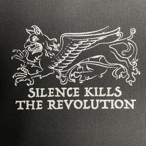 Peut inclure: Écusson en tissu noir avec une illustration blanche d'un griffon, créature mythique avec un corps de lion et une tête et des ailes d'aigle. Le texte "SILENCE KILLS THE REVOLUTION" est imprimé en dessous.