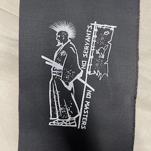 Puede incluir: Parche de tela negra con un gráfico blanco de una figura tipo samurái con cresta y espadas. El parche incluye el texto "NO SERVANTS NO MASTERS" y una bandera con una ilustración de gato.