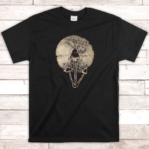 Puede incluir: Camiseta negra con un estampado dorado de un hongo con un sombrero grande y un patrón radiante a su alrededor.