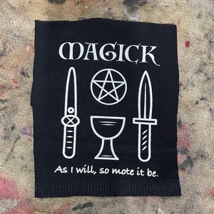 May include: Black patch with white text and symbols. The word "MAGICK" is at the top, with a pentagram, chalice, and two daggers below. The phrase "As I will, so mote it be" is at the bottom.