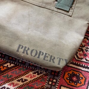 May include: A white ceramic mug with a black handle and the text "But First, Coffee" in a bold, black font. The mug is set against a blurred background, suggesting a cozy setting.