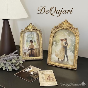 Könnte beinhalten: Zwei verzierte goldene Bilderrahmen mit gewölbten Oberteilen. Einer zeigt eine Frau am Fenster, der andere ein tanzendes Paar. Die Rahmen stehen auf einer dunklen Oberfläche mit dem Text "DeQajari" und "Vintage Treasures Co."
