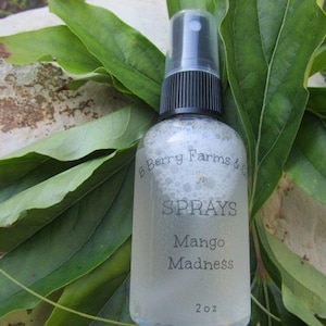 May include: A clear glass bottle with a black spray top and a white label that reads "B Berry Farms & Co. SPRAYS Mango Madness 2 oz."