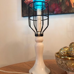 May include: A white ceramic table lamp with a black wire cage shade. The shade has a blue glass globe on top. The lamp is on a wooden table.