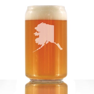 May include: A clear glass beer can with a white outline of the state of Alaska on the side. The can is filled with a light amber colored beer and has a white head of foam.