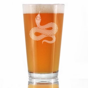 May include: A pint glass with a white snake design, filled with beer. The beer is a light orange colour with a foamy head. The snake design is etched onto the glass, adding a decorative element.