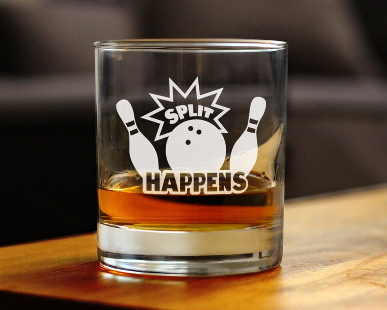 Pode incluir: Um copo de vidro transparente com um desenho branco de dois pinos de boliche e uma bola de boliche com o texto "SPLIT HAPPENS".