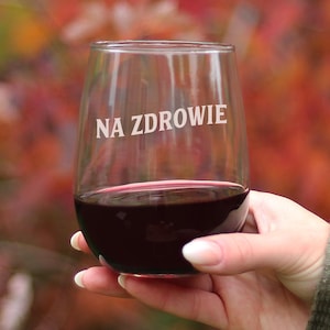 Puede incluir: Una copa de vino sin tallo de vidrio transparente con el texto "NA ZDROWIE" grabado en el lateral. La copa está llena de vino tinto y la sostiene una mano.