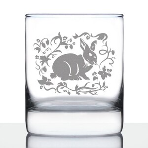 May include: A clear glass tumbler with a gray etched design of a rabbit in a floral wreath.