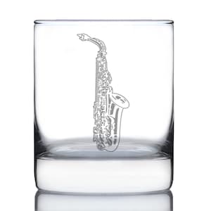 Könnte beinhalten: Ein klares, zylindrisches Whiskyglas mit einem detaillierten, geätzten Saxophon-Design. Das Musikinstrument ist vertikal dargestellt und zeigt seine komplizierten Klappen und den Schalltrichter. Das Glas eignet sich zum Servieren von Whisky oder anderen Getränken.