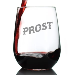 May include: A stemless wine glass with the word "PROST" in gray lettering. Dark red wine is being poured into the glass, filling it. The background is white.