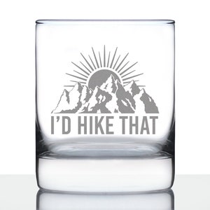 Puede incluir: Un vaso de vidrio transparente con una silueta de montaña gris y un gráfico de sol. El texto "I'd Hike That" está impreso debajo del gráfico.