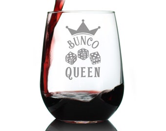Puede incluir: Una copa de vino de vidrio transparente con una corona y el texto "Bunco Queen" y tres dados impresos en ella. La copa está llena de vino tinto.