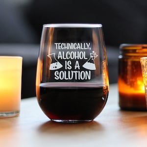 May include: A clear glass wine glass with the text "Technically, Alcohol is a Solution" etched on the side. The glass is filled with red wine and is sitting on a wooden table.