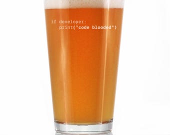 May include: A pint glass filled with beer, featuring a foamy head. The glass has the text "if developer: print("code blooded")" printed on it. The beer is a light amber color.