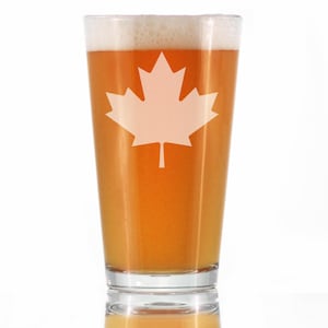 May include: A tall glass beer mug with a white maple leaf design. The mug is filled with a light amber colored beer.