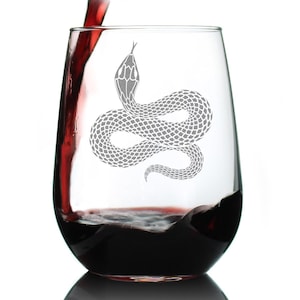 May include: A stemless wine glass with a gray snake design. The glass is filled with red wine, with more wine being poured from above. The snake is coiled and detailed, with a textured pattern. The glass is clear, and the background is white.