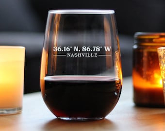May include: A clear glass wine glass with a red wine inside. The glass has the text "36.16° N. 86.78° W - NASHVILLE -" etched on the side.