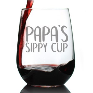 May include: A clear glass wine glass with the text "Papa's Sippy Cup" printed on the side. Red wine is being poured into the glass.