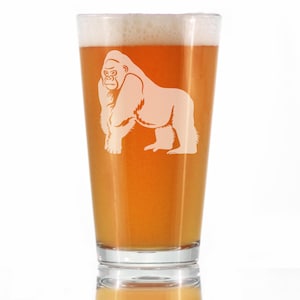 May include: A clear glass beer pint with a white gorilla graphic etched on the side. The glass is filled with a light amber colored beer.