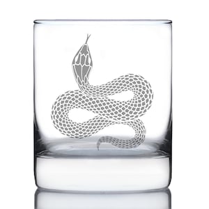 May include: A clear glass tumbler with a gray snake design. The snake is coiled and has a detailed scale pattern. The glass is a standard size for drinking beverages.