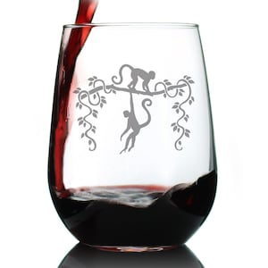 May include: A clear glass wine glass with a design of two monkeys swinging on vines. The glass is filled with red wine.