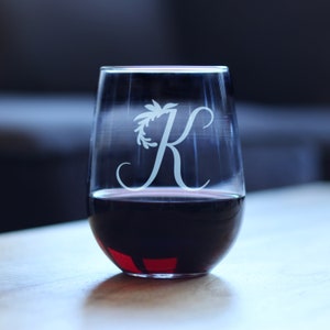 Può includere: Un bicchiere di vino senza gambo in vetro trasparente con un design inciso bianco di una ghirlanda di foglie che circonda la lettera "K". Il bicchiere è pieno di vino rosso.