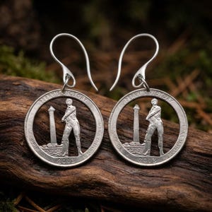 May include: A pair of silver-toned drop earrings crafted from cut-out 2013 Perry's Victory Ohio quarters. Each earring features a central figure standing beside a tall monument, with the text PERRY'S VICTORY and E PLURIBUS UNUM visible.