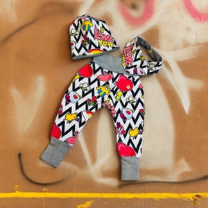 Könnte beinhalten: Ein Baby-Outfit-Set mit Mütze, Stirnband und Hose. Die Artikel haben ein schwarz-weißes Zickzackmuster mit bunten Herzen, Blumen und dem Text "Love You". Die Bündchen und der Bund sind grau.