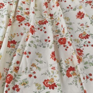 May include: A cream-colored fabric featuring a repeating floral pattern with red, orange, and yellow blossoms interspersed with small green leaves and thin, winding stems. The textile displays a dense arrangement of botanical elements throughout.