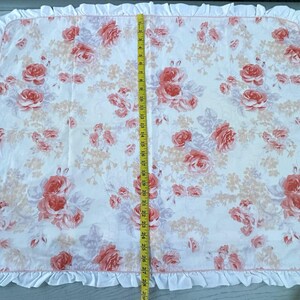 May include: A rectangular fabric featuring a floral pattern with a white base and pink roses and peach-colored flowers. The fabric is approximately 74 cm long, with a ruffled edge.
