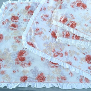 May include: White bedding set featuring a rose floral pattern in peach and pink hues. The set includes a blanket and pillowcases, all finished with a ruffled edge.