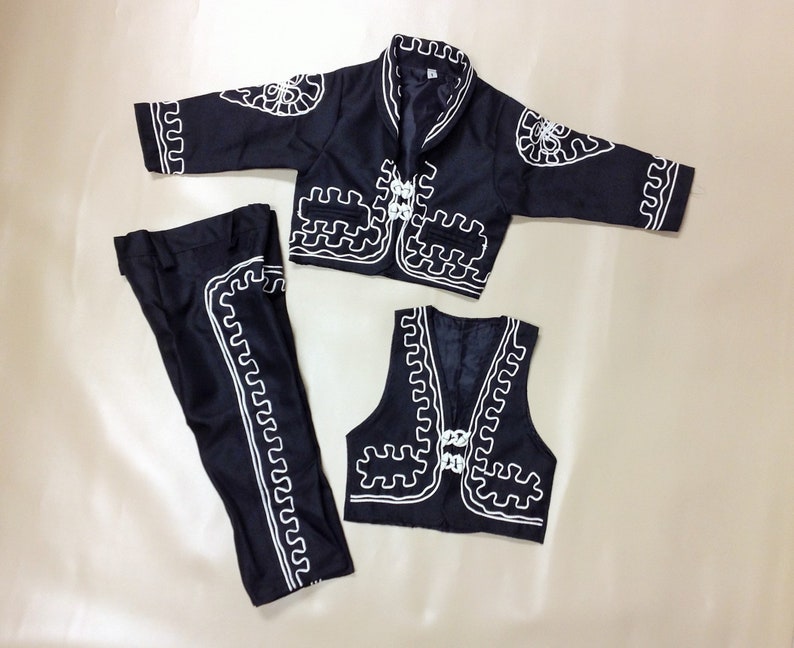 Puede incluir: Un traje de charro negro y blanco para un ni&ntilde;o. El traje incluye una chaqueta, un chaleco y pantalones. La chaqueta y el chaleco tienen dise&ntilde;os bordados en blanco. Los pantalones tienen dise&ntilde;os bordados en blanco a los lados.