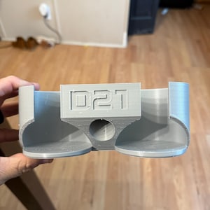 May include: A gray 3D printed cup holder with two slots and the text "D21" on the front.