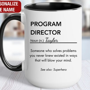 May include: White ceramic mug with a black handle and black rim. The mug has a black and white design that reads "PROGRAM DIRECTOR Noun (n.) Taylor Someone who solves problems you never knew existed in ways that will blow your mind. See also: Superhero"