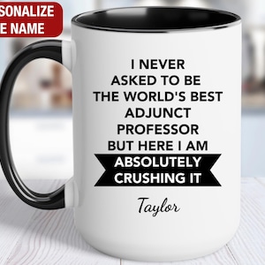 May include: White coffee mug with a black rim and handle. The mug has black text that reads "I never asked to be the world's best adjunct professor but here I am absolutely crushing it". The name "Taylor" is printed below the text.