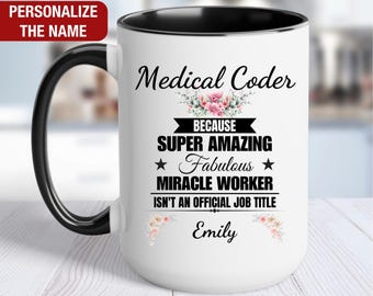 May include: White ceramic coffee mug with a black rim and handle. The mug features a floral design and the text "Medical Coder because super amazing fabulous miracle worker isn't an official job title Emily".