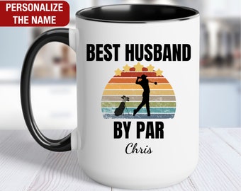 May include: White ceramic coffee mug with a black rim and handle. The mug features a retro-style graphic of a golfer with a golf bag and the text "BEST HUSBAND BY PAR Chris".