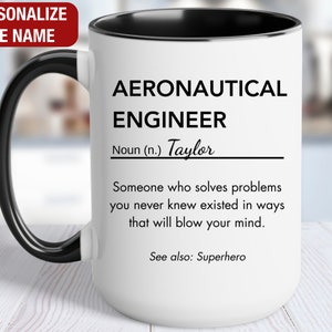 May include: White ceramic mug with a black handle and black rim. The mug has a black and white design that reads "Aeronautical Engineer Noun (n.) Taylor Someone who solves problems you never knew existed in ways that will blow your mind. See also: Superhero"