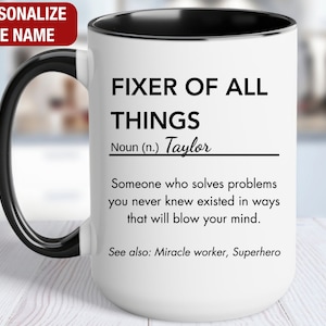 May include: White ceramic mug with a black handle and rim. The mug has black text that reads "Fixer of All Things" and "Noun (n.) Taylor". Below the text is a definition that reads "Someone who solves problems you never knew existed in ways that will blow your mind." The text "See also: Miracle worker, Superhero" is printed below the definition.