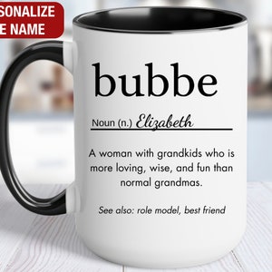 May include: White ceramic mug with a black handle and rim. The mug has a black and white design that reads "bubbe" with a definition and the name "Elizabeth".