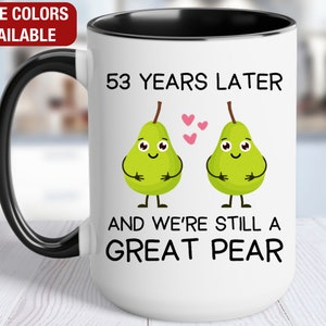 May include: White ceramic mug with a black handle and rim. The mug has a graphic of two green pears with faces and the text "53 Years Later and We're Still a Great Pear".
