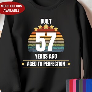 May include: Black sweatshirt with a vintage-style graphic that says "Built 57 Years Ago Aged to Perfection". The graphic features a rainbow-colored sunset with five gold stars.