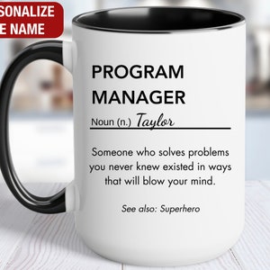 May include: White ceramic mug with a black handle and black rim. The mug has a black and white design that reads "PROGRAM MANAGER Noun (n.) Taylor Someone who solves problems you never knew existed in ways that will blow your mind. See also: Superhero"