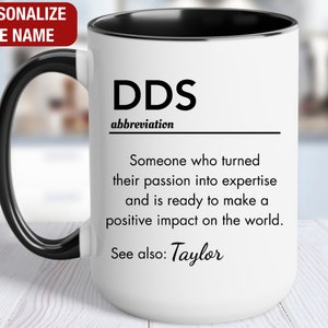 May include: White ceramic mug with a black handle and black rim. The mug has black text that reads "DDS abbreviation Someone who turned their passion into expertise and is ready to make a positive impact on the world. See also: Taylor"