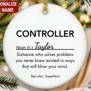 May include: A white ceramic Christmas ornament with the word "CONTROLLER" in bold black letters. Below, the name "Taylor" is written in cursive. The ornament includes the definition of a controller and the phrase "See also: Superhero."