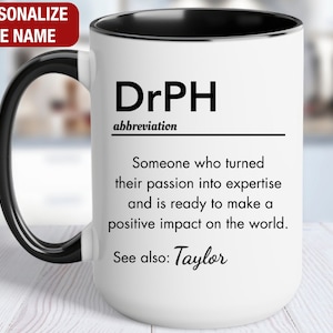 May include: White ceramic mug with a black handle and black rim. The mug has a black and white design that reads "DrPH abbreviation Someone who turned their passion into expertise and is ready to make a positive impact on the world. See also: Taylor"