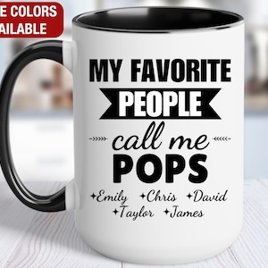 May include: White ceramic coffee mug with a black rim and handle. The mug has black text that reads "My Favorite People Call Me Pops" with a black arrow pointing to the left and right of the text. Below the text are six names: Emily, Chris, David, Taylor, and James.