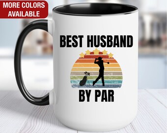 May include: White ceramic coffee mug with a black rim and handle. The mug features a retro-style graphic of a golfer with a golf bag and the text "Best Husband By Par".